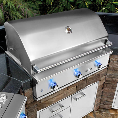 Stainless steel grill on a stone outdoor kitchen counter with greenery in the background