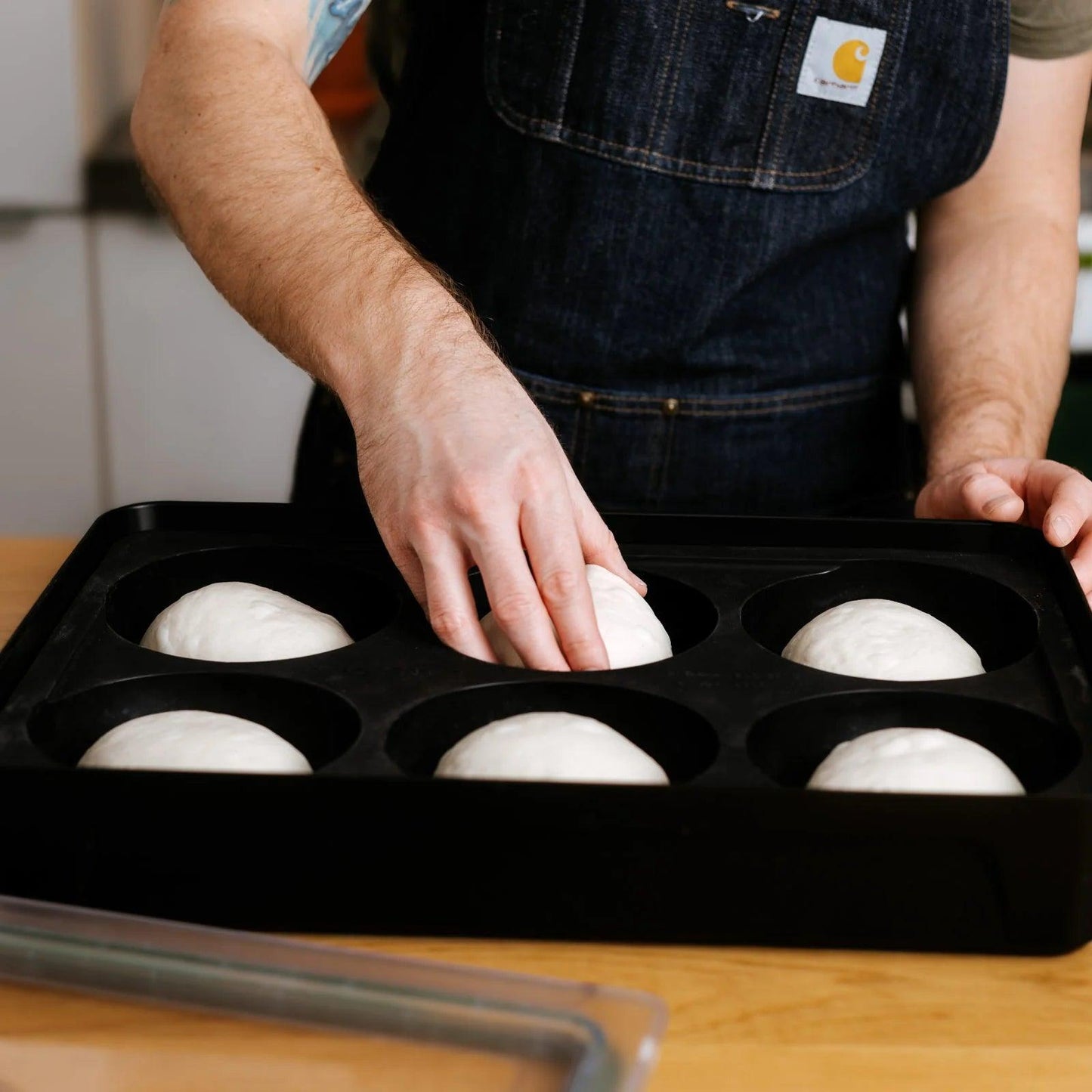 Person placing dough balls into a Gozney Dough Tray  on a wooden surface.