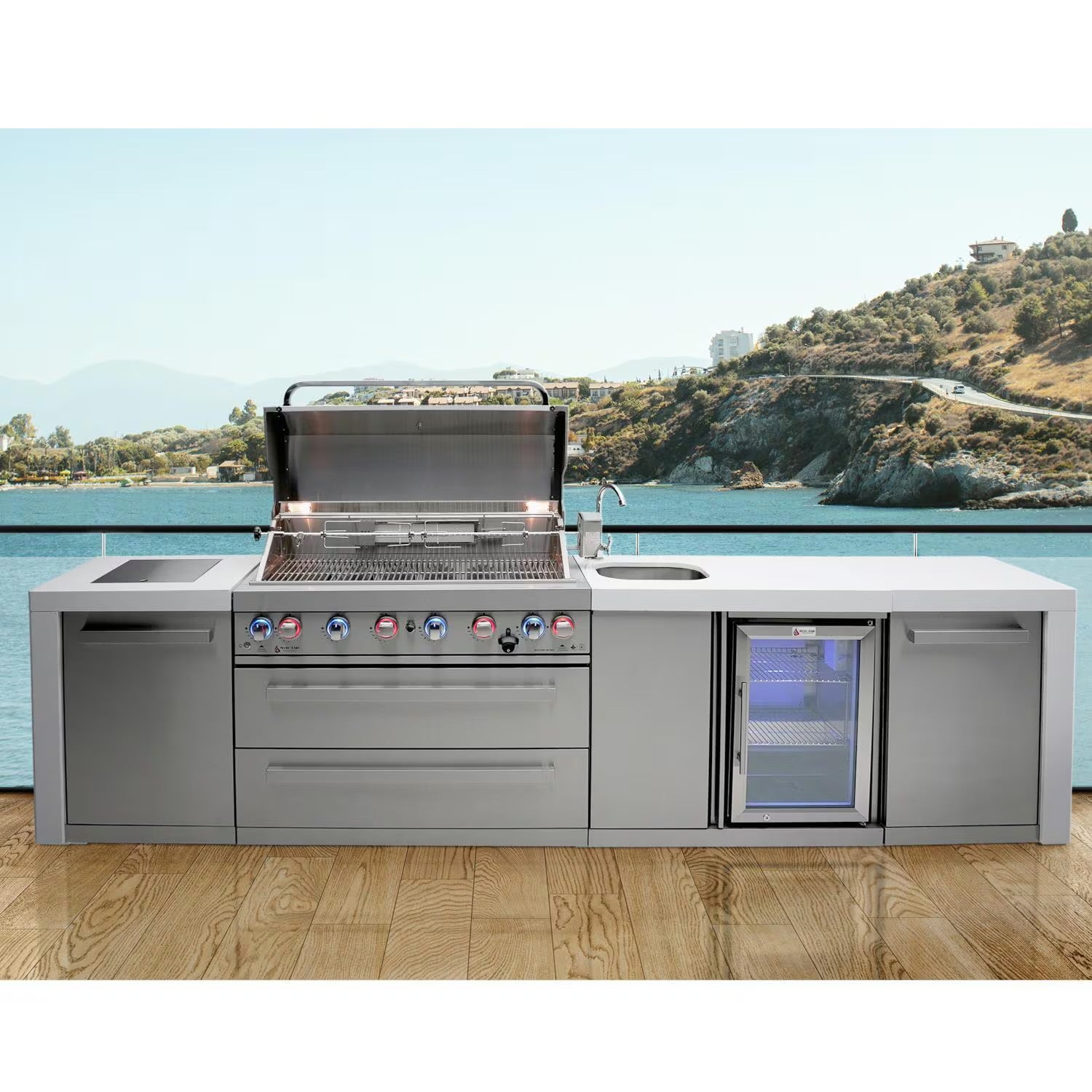Mont Alpi Stainless steel outdoor kitchen with grill and refrigerator by a scenic waterfront.