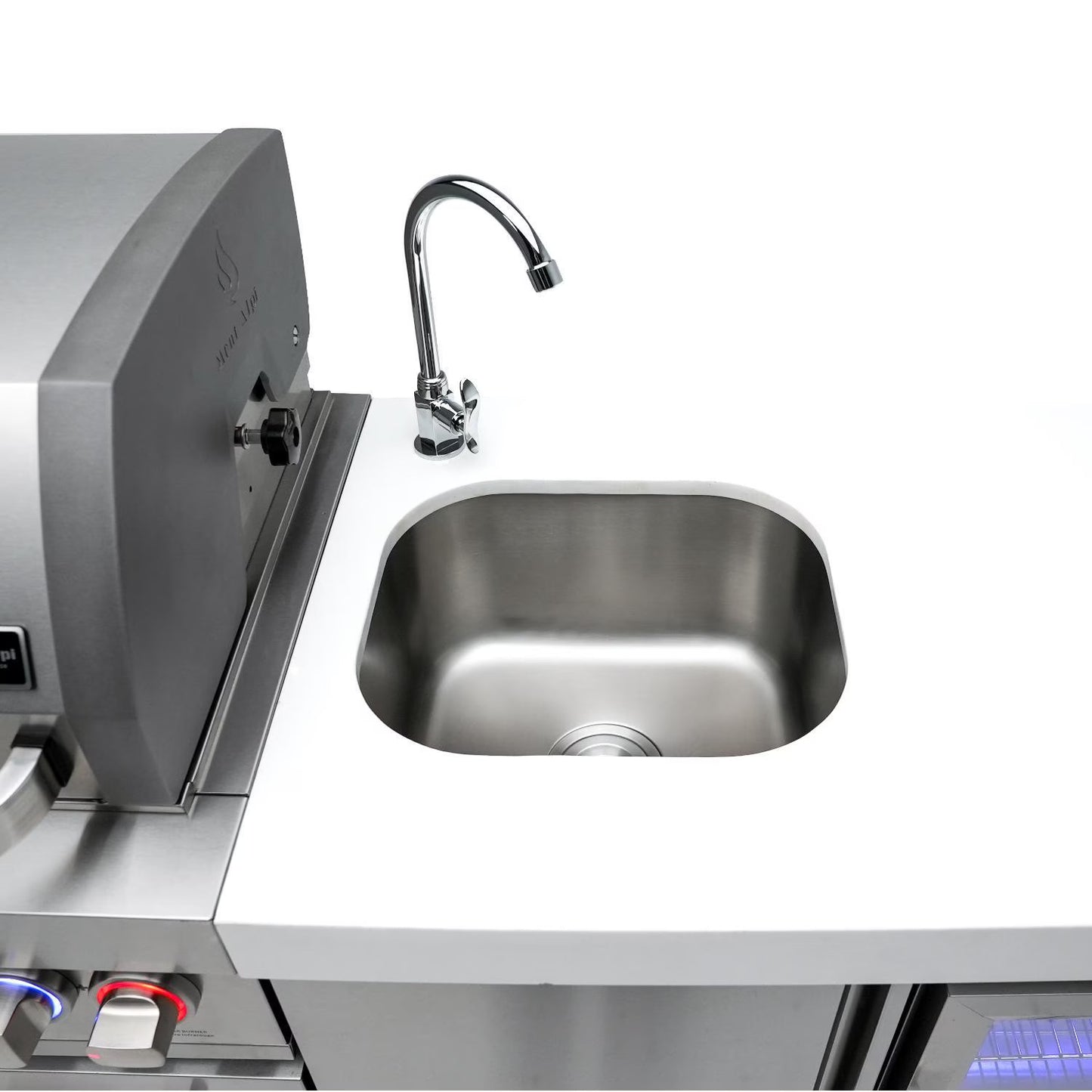 Mont Alpi Stainless steel sink and faucet on a kitchen counter with a grill in the background.