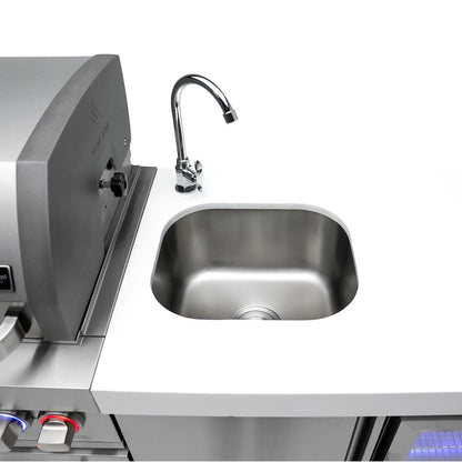 Mont Alpi Stainless steel sink and faucet on a kitchen counter with a grill in the background.