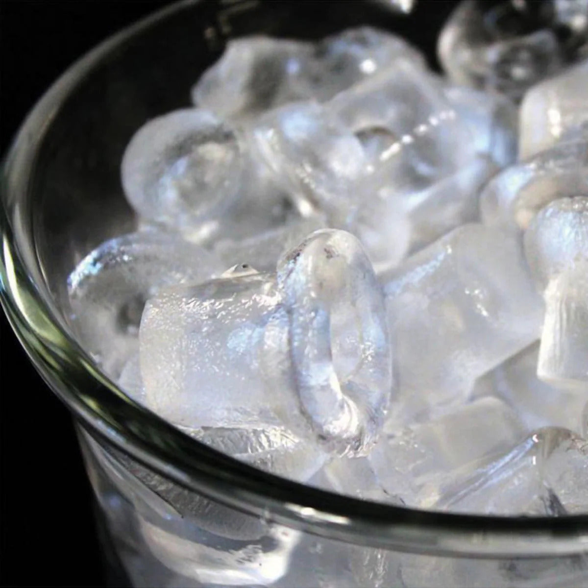 Clear glass bowl filled with ice cubes on a dark background