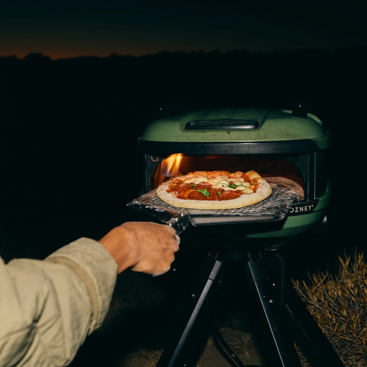 Person cooking a pizza in a portable outdoor oven at night.