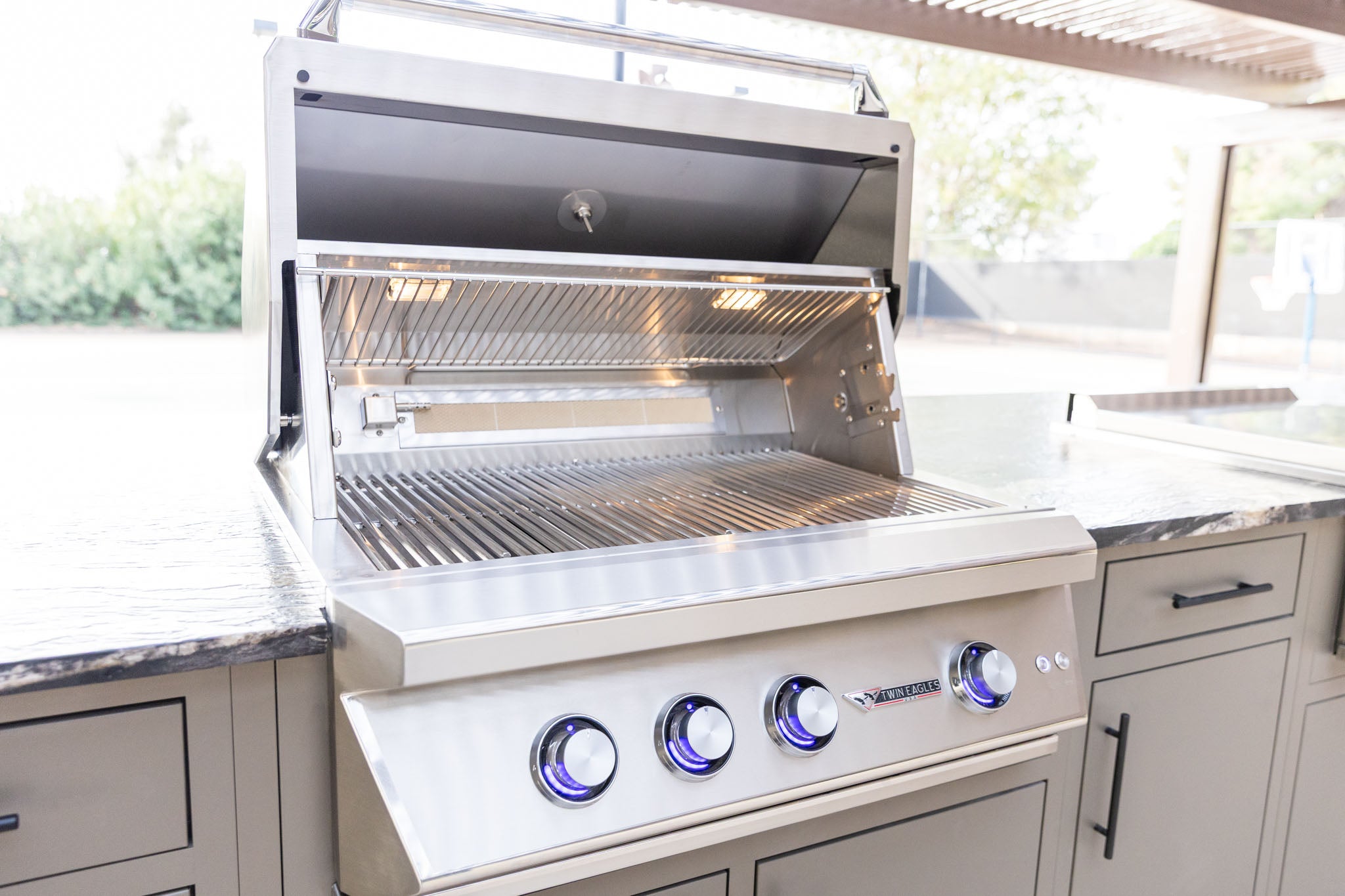 Built-in stainless steel gas grill with lit burner knobs in a custom outdoor kitchen island - Phoenix, AZ